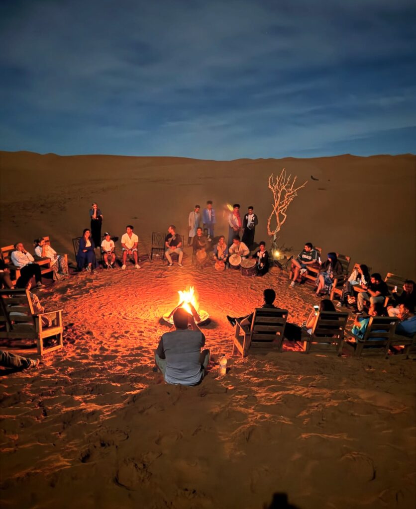 A group of people gathered around a fire in a desert camp during the 2 days from Marrakech to Zagora tour, enjoying a memorable evening together.