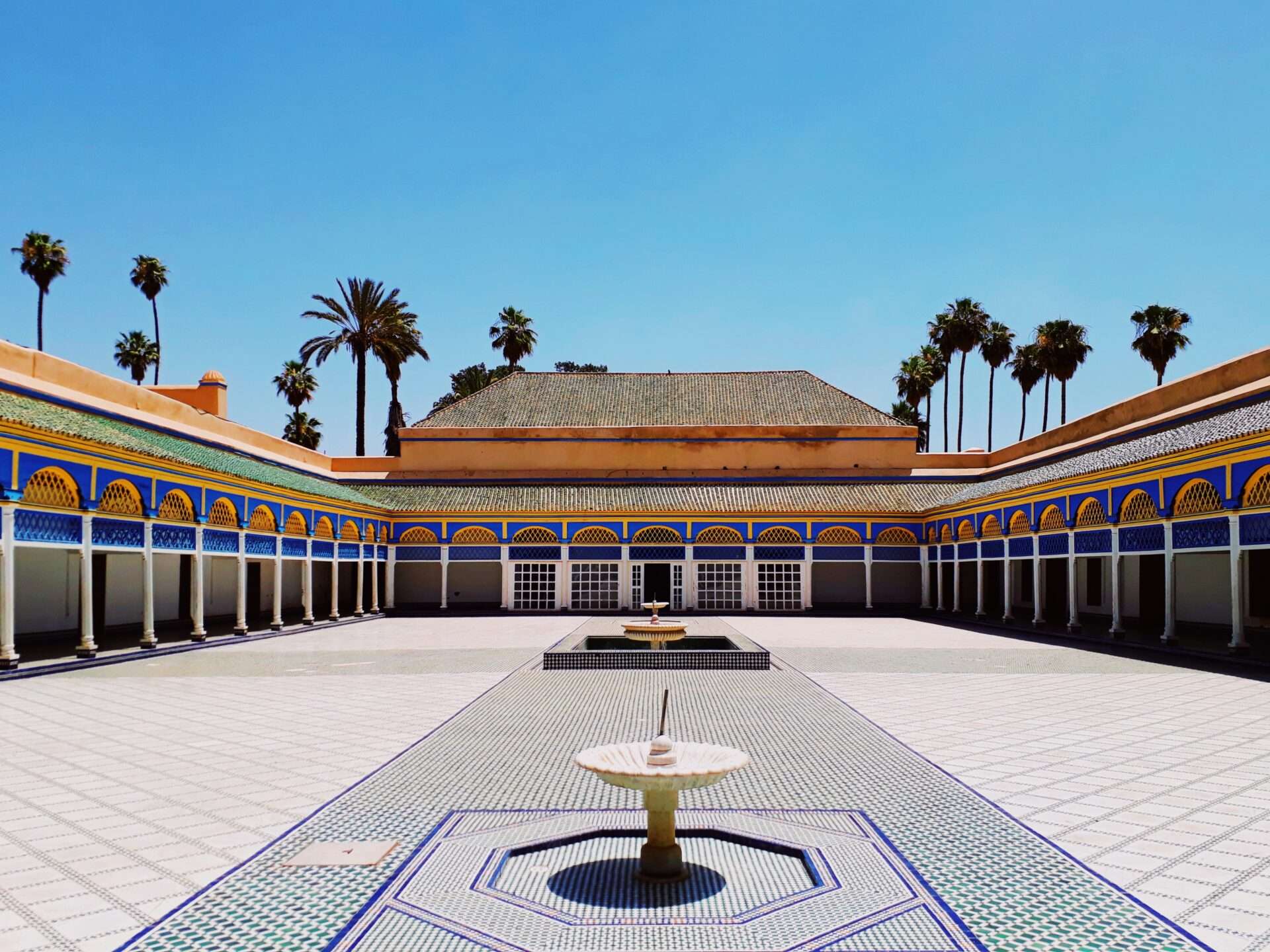 Intricately decorated courtyard of Bahia Palace in Marrakech, featuring zellige tilework, carved wooden ceilings, and arched doorways.