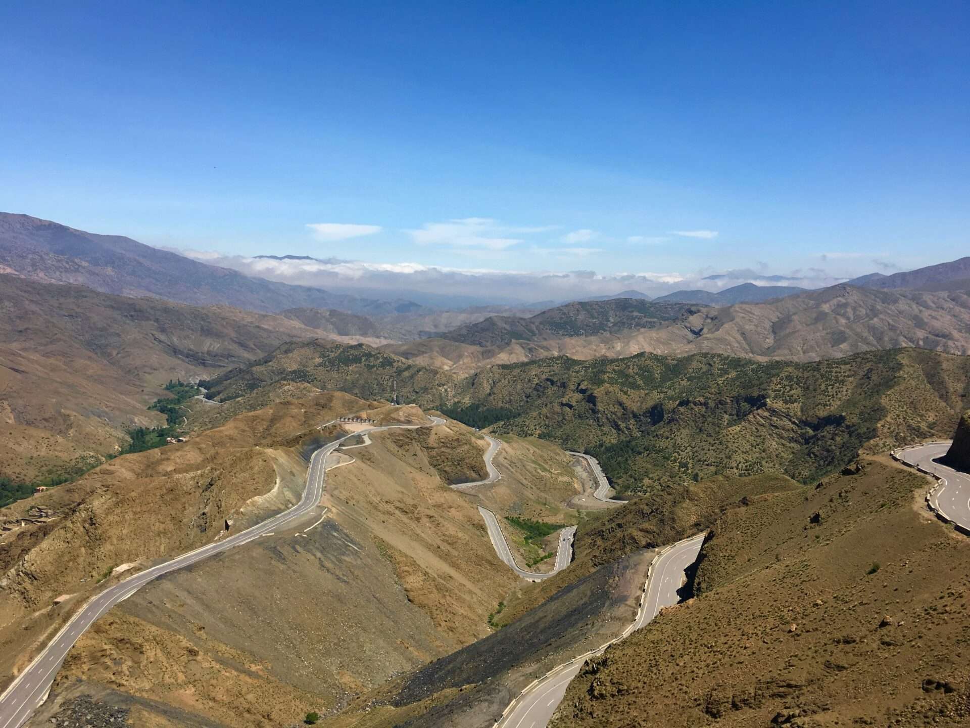Winding road through the rugged Atlas Mountains of Morocco, surrounded by dramatic peaks, valleys, and scattered Berber villages.
