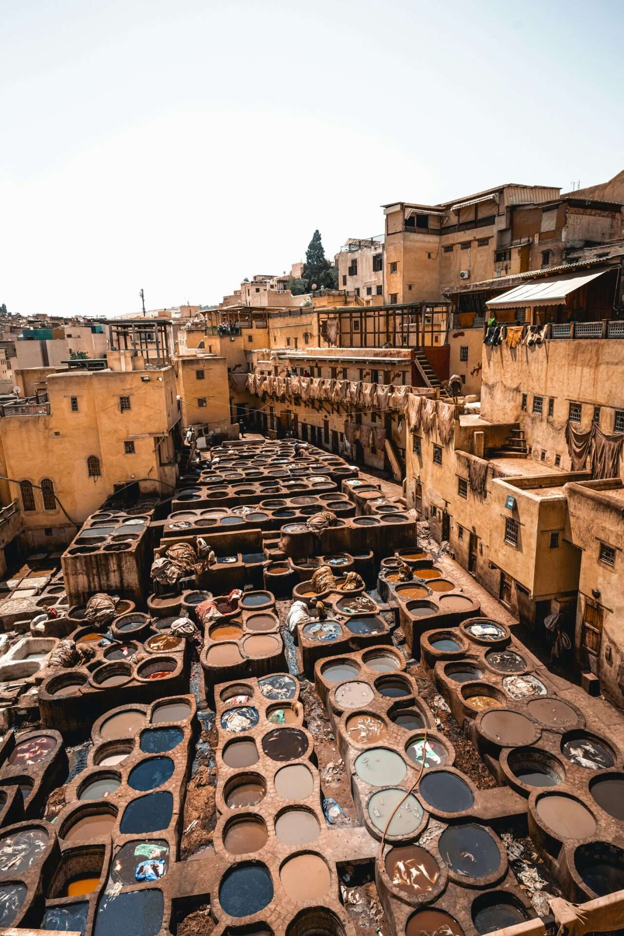 Aerial view of Chouara Tanneries in Fes, Morocco, showing stone vats filled with vibrant dyes and workers treating leather by hand.