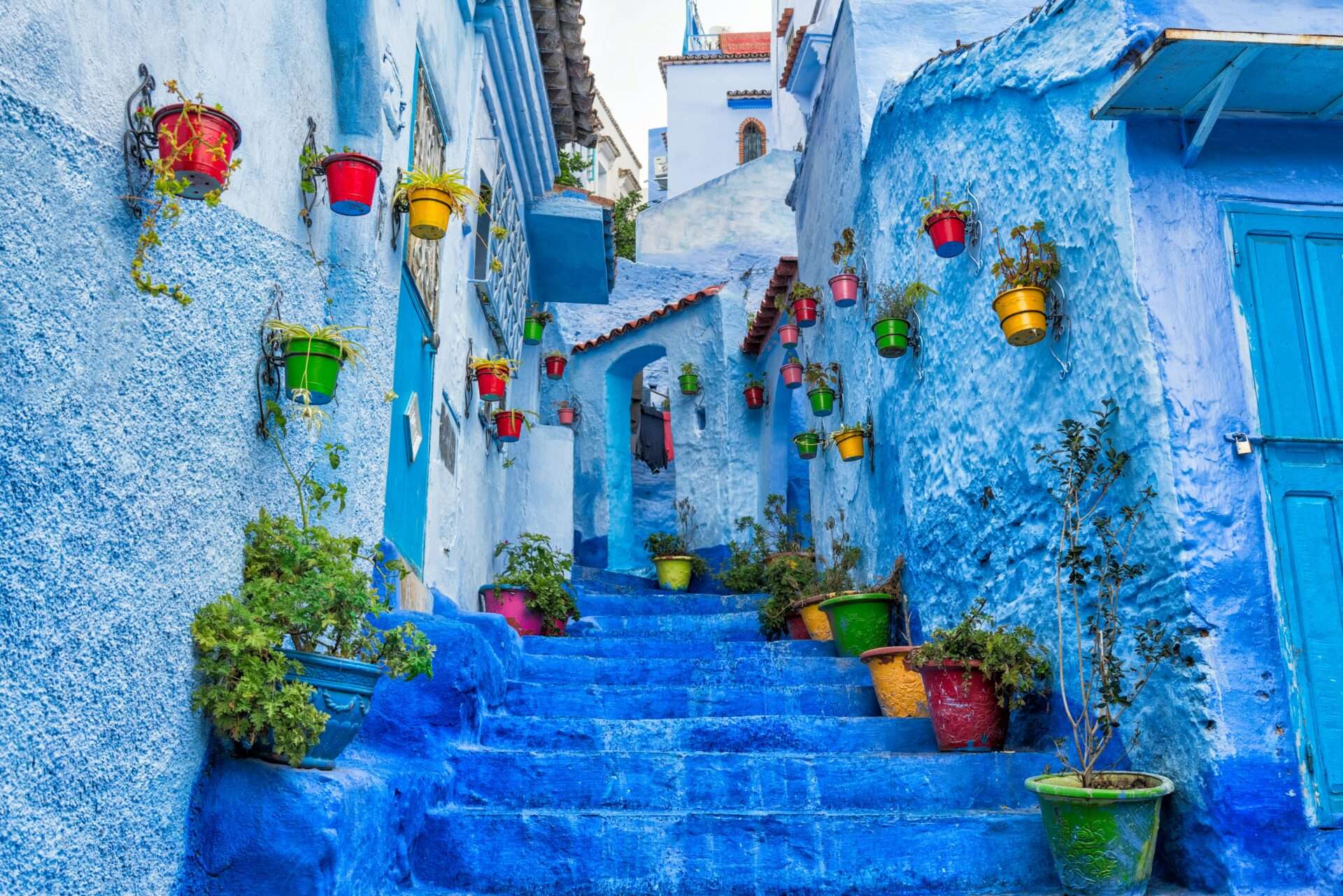 Scenic view of Chefchaouen, the Blue City of Morocco, with narrow streets, blue-washed buildings, and colorful flower pots.