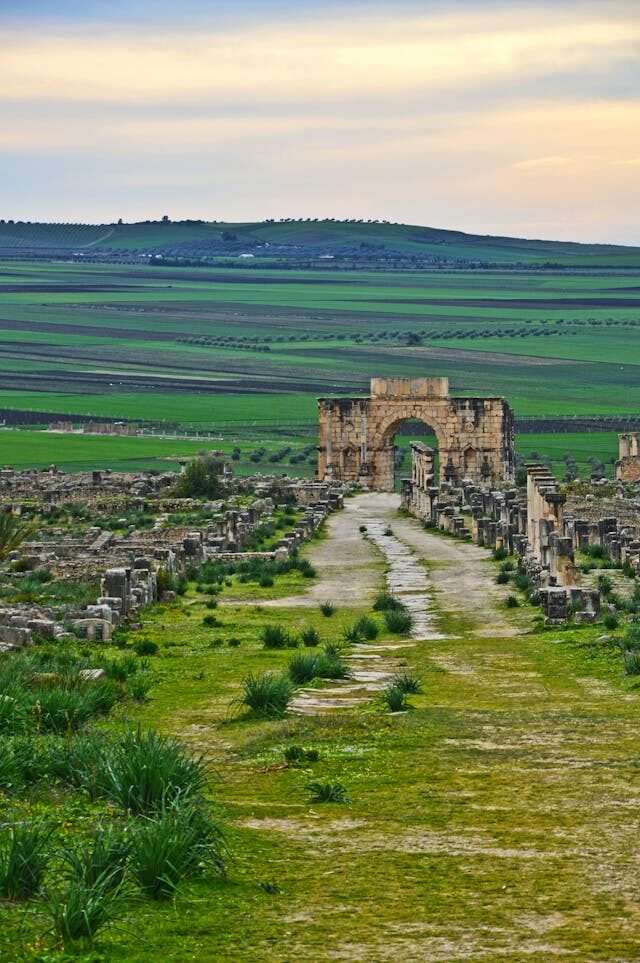 Ancient Roman ruins of Volubilis in Morocco with stone columns, mosaics, and distant hillside views