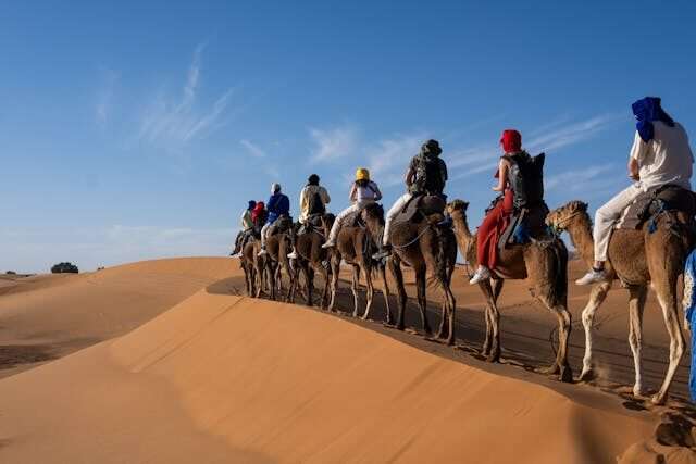 Camel trek through the golden dunes of the Sahara Desert in Merzouga, Morocco – travelers riding camels at sunset
